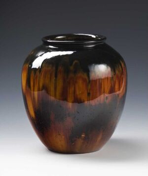  A glossy, rounded vase with a small opening, featuring a transition from deep black at the top to streaks of amber brown resembling wood patterns, set against a soft gray background. Artist name and title are unknown.