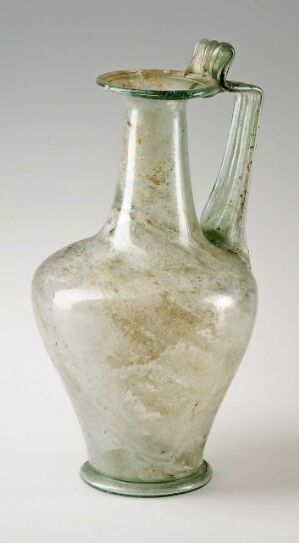  Antique pale green glass vessel with a rounded base, narrow neck, flared rim, and side handle, showcasing a cloudy marbled pattern against a light grey background.