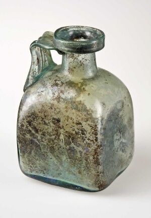  Antique aquamarine glass bottle with a looped handle and weathered appearance, featuring cloudy glass with variations in color intensity and mottled brownish stains indicative of age.