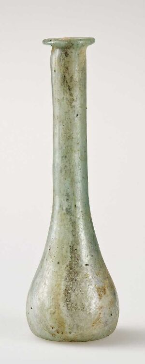  An antique green glass vase with a mottled pattern, showing a spectrum of green shades, standing against an off-white background. The vase has a narrow neck and a flared opening. Artistname and title are unknown.