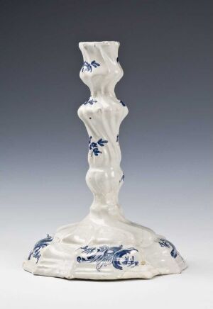  A white porcelain candlestick with blue floral patterns featuring an organic, stalk-like design with three bulbous sections on its stem, set against a soft grey backdrop.