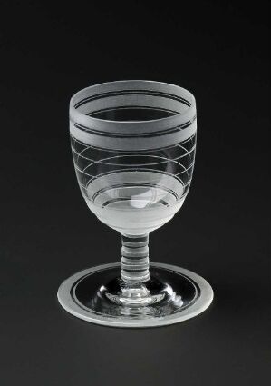 
 An engraved blown glass goblet by artist Sverre Pettersen displayed against a dark background, featuring a solid base, an engraved stem with faceted reflections, and a bowl with horizontal engraved lines.