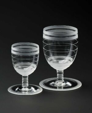  Two clear glass goblets with engraved circular grooves, designed by Karen Jacobsen, are presented against a dark background, showcasing their elegant design and craftsmanship.