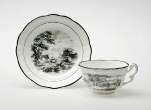  A porcelain teacup and saucer set with monochromatic landscape scenes in shades of gray on a plain background. The cup has a handle on the right side, and both pieces have a thin decorative border.