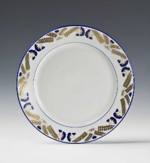 
 A round ceramic plate with a white center and a rim decorated with cobalt blue and golden brown foliage motifs, set against a light grey background.