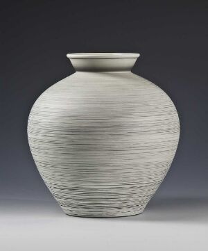  A textured feldspar porcelain vase designed by Nora Gulbrandsen with a bulbous body, short neck, and horizontal linear grooves, set against a gradient background ranging from dark to light gray.