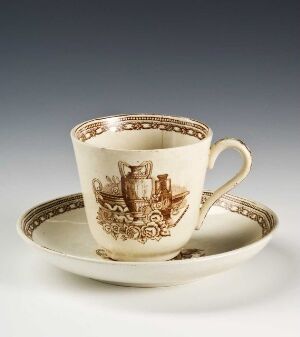  An elegant, off-white porcelain tea cup with gold decorative patterns sitting on a matching saucer, presented against a neutral background.