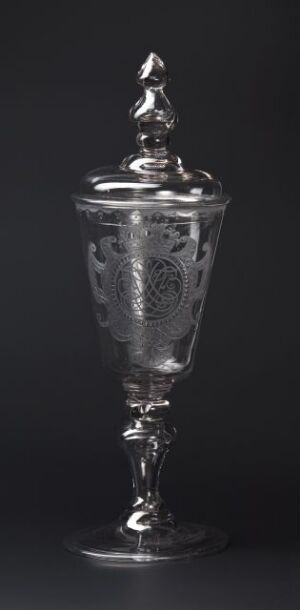  An ornate silver goblet with an embellished lid and detailed engravings, set against a dark background.