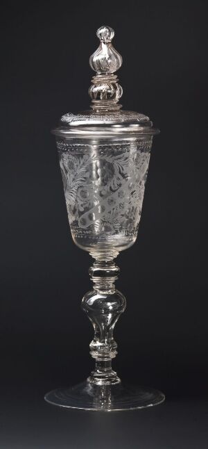  An elaborate crystal goblet with a lid and detailed etched patterns set against a dark background. The goblet displays expert craftsmanship and intricate design, with the material's reflective quality catching the light.