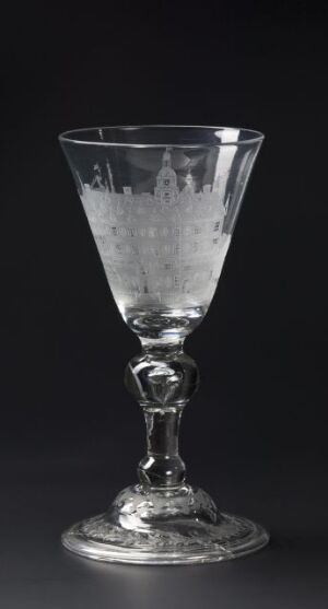  An antique glass goblet with an engraved pattern and a stem featuring a small sculpted figure against a solid dark background. The artistname and title are unknown.