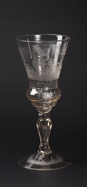  An ornate, clear glass goblet with intricate engravings on the bowl and a detailed stem, set against a dark background.