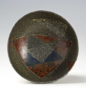  An antique spherical bowl with a weathered surface set against a light gray background, featuring a decorative triangle within a triangle motif in the center, with colors of reddish-brown, dark blue, and gray. Artist name and title are unknown.