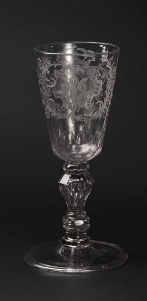  An ornate clear glass with etched floral patterns stands against a dark background, showcasing its reflective surface and intricate design.