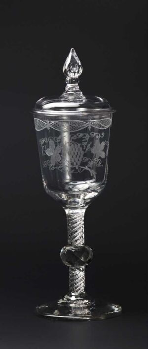  A monochromatic image of an ornate glass goblet with a lid, featuring etched patterns, against a black background. The goblet has a circular base, a slender stem with decorative elements, a cylindrical bowl with intricate designs, and a pointed finial on the lid. Artist name and title remain unknown.