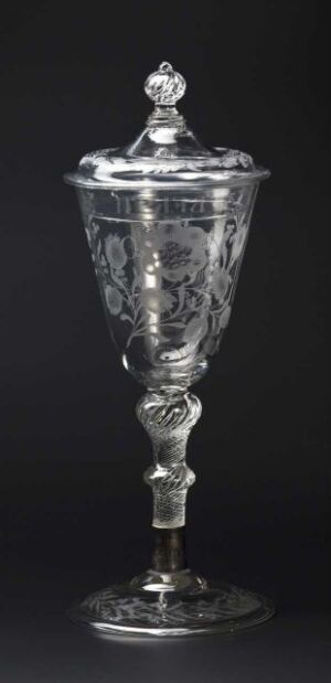  An elegant silver standing cup with cover, featuring detailed engraving of floral designs, displayed against a black background.