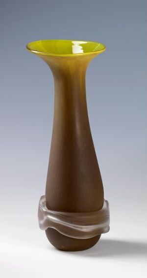  "Åpent frø med frossent bånd" by Ulla-Mari Brantenberg, a blown glass piece with a clear, swirled base transitioning to a smoky brown body and a bright yellow flared opening, showcasing expert craftsmanship in glassmaking techniques.