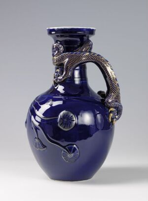  An elegant cobalt blue vase with a serpentine metallic handle and multiple clear round inclusions on its body, set against a neutral gray background. Artist name and title are unknown.