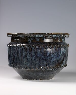  A textured ceramic pot with a fluted body, glazed in shades of deep to lighter blue with a rim showing hints of brown and green, set against a neutral grey background.