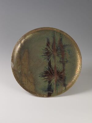  A round ceramic plate with an olive green and brown mottled background, adorned with a streak of dark brushwork overlaid by delicate reddish-brown pine-like branches and dotted with gold around its rim. Artist name and title unknown.