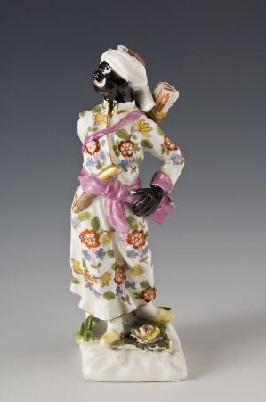  Porcelain figurine of a traditional Japanese woman in a floral kimono with a pink obi sash, standing on a base resembling a grassy mound with flowers.