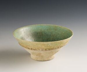  A handcrafted ceramic bowl with a glossy green interior that transitions to a textured, earthy band and a beige exterior, set against a soft gray to white gradient background.