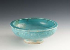  A small, antique turquoise-glazed ceramic bowl with textured relief patterns on the sides, with the unglazed beige base showing at the bottom, against a grey background.