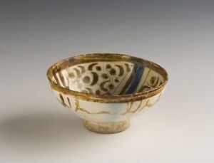  An ornate small bowl with a tapering base and a wide, open top, featuring a quarter segment of deep cobalt blue and the remainder decorated with circular brown patterns and gold accent lines, set against a light grey background.