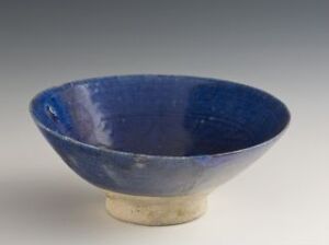  A handcrafted ceramic bowl with a rich cobalt blue glaze inside and a natural, raw ceramic exterior standing on a narrow unglazed foot against a neutral gradient background.