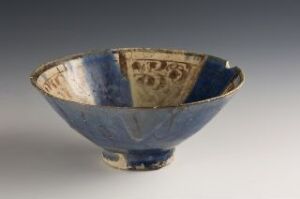  Antique ceramic bowl with a flared rim and a small foot, featuring a cobalt blue exterior and an interior adorned with golden-brown calligraphy and patterns on a lighter blue background.