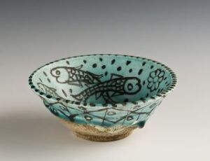 
 A small ceramic bowl with a beige to dark gradient exterior and a decorated interior featuring teal or turquoise patterns, including two stylized fish surrounded by floral and geometric motifs, all against a neutral gray background.