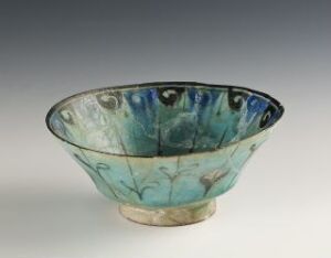  An ornamental bowl with a flared rim, featuring a blue and green floral pattern on the inside, set against a neutral gray background. The bowl rests on a small rounded base, suggesting a blend of functionality and artistry.