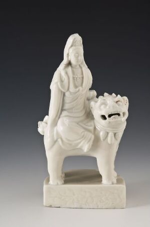  An off-white statuette depicting a serene figure clothed in traditional Asian attire, sitting on a mythological lion-like creature, against a neutral background.