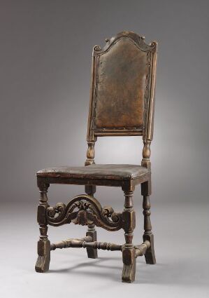  Antique wooden chair with elaborate baroque carvings in dark brown wood, featuring a high back with faded upholstery, ornate stretchers, and claw-and-ball feet, set against a neutral gray background.