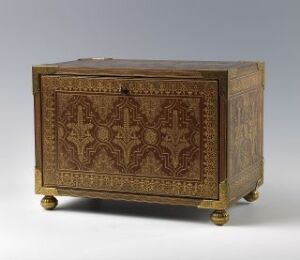  An antique wooden chest with intricate pale golden inlay patterns, including a symmetrical cross on the front, sitting on four lustrous golden feet against a gray background.