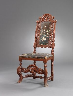  An antique carved wooden chair with an upholstered backrest and seat featuring floral embroidery, set against a neutral grey background.