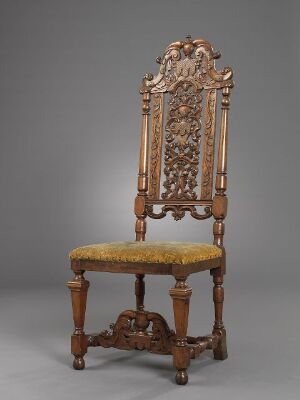  An antique wooden chair with a tall, intricately carved backrest and golden upholstery against a neutral gray background.