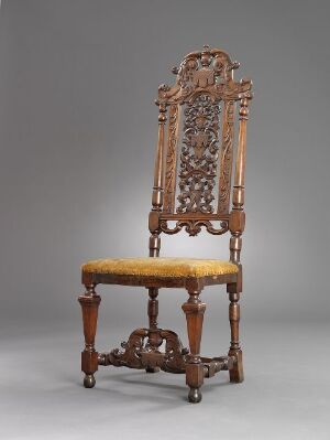  An antique wooden chair with elaborate openwork carving on the tall backrest and a mustard yellow upholstered seat, set against a neutral grey background.