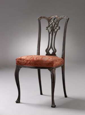  An antique-style chair with a high, intricately designed wooden back and a plush rusty-pink upholstered seat, set against a simple gray background.