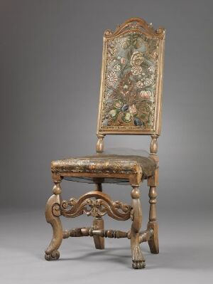  An antique wooden chair with elaborate carvings in a golden brown color, featuring a tall, rectangular, floral-patterned upholstered backrest and seat, set against a neutral gray background.