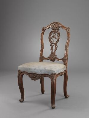  An antique chair with intricate wood carvings and an upholstered off-white seat, set against a simple gray background.