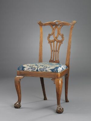  An antique chair with a golden-brown wood finish and clawed feet, featuring a high, curvy backrest with scroll detailing and a floral patterned seat in shades of blue and green.