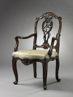  An antique wooden armchair with elaborate carvings and a pale upholstered seat against a muted background.