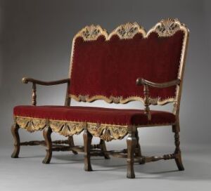  An elaborate antique gilded settee with deep red upholstery and ornate wooden carvings on a gray background.