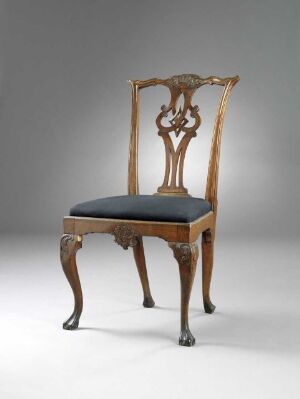  Antique wooden chair with a sculpted backrest featuring a central shell motif, upholstered in deep blue fabric, set against a light gray background.