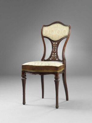  An antique chair with a curved backrest featuring a central flower-like carving, upholstered in creamy fabric, and made from dark, glossy wood, set against a plain gray background.