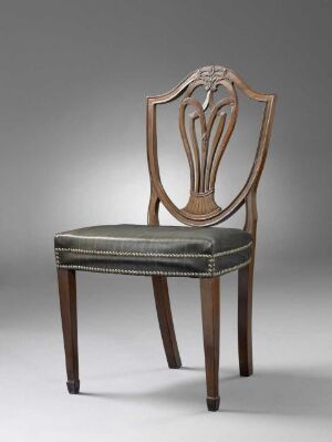  A varnished mahogany chair with intricate carved detailing in the shape of three converging leaves or feathers on the backrest, and a firmly upholstered seat cushion with a decorated border, set against a gray background.