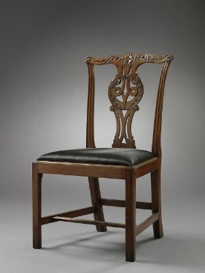  An elegant wooden chair with an intricately carved backrest and a black leather seat cushion, set against a soft gray background.