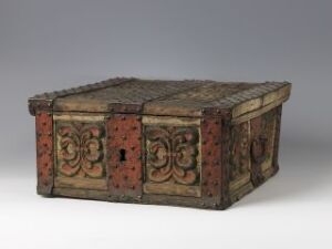  An antique wooden chest with ornate carvings and metal reinforcements, featuring a curved top, keyhole, and a pattern of rusty metal studs, displayed against a light grey background.