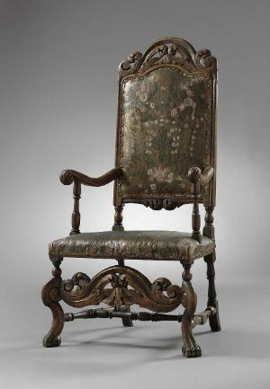  An antique wooden chair with elaborate carvings and faded green upholstery set against a light gray background.