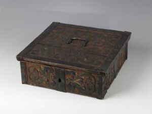  An antique wooden box with intricate carvings and faded floral patterns in shades of red, green, and yellow, featuring a metal clasp on the front and a rectangular handle on the lid, displayed against a neutral background.